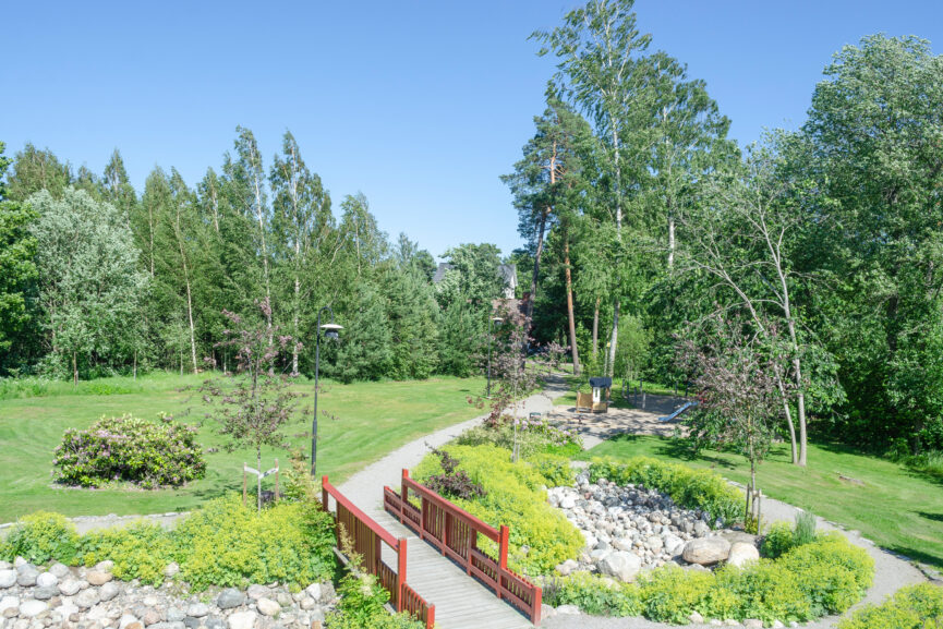 grönt parkområde med lekplats och röd trädbro över stenparti